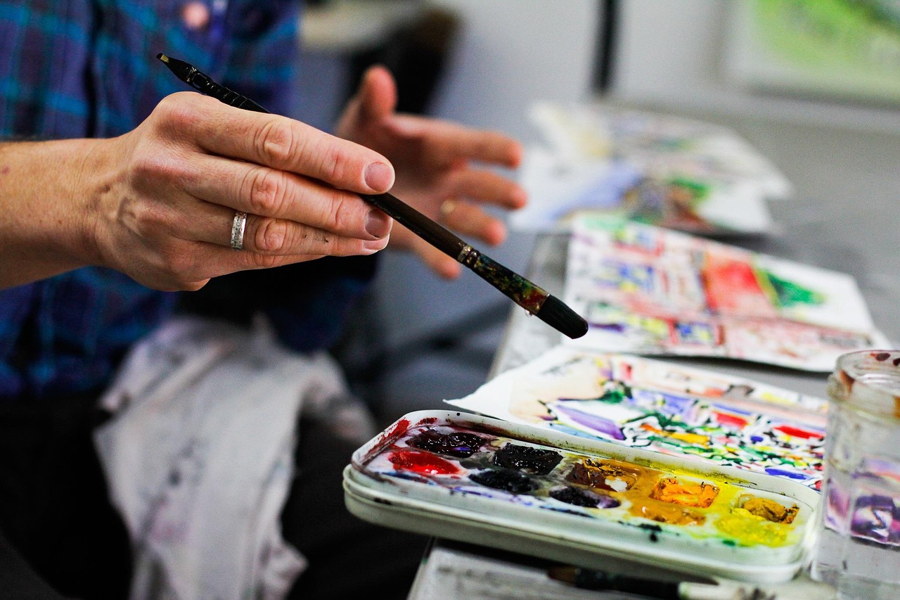 An artist's hand holding a paintbrush over a paint palette.
